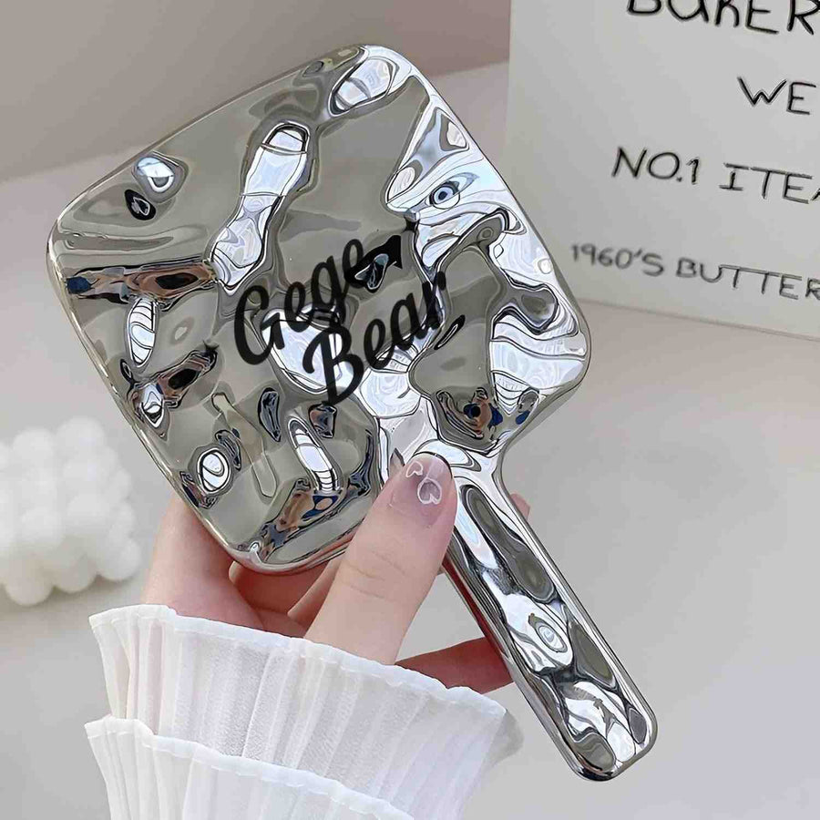 Silver marbled hand mirror with 'Gege Bear' branding held by a hand.