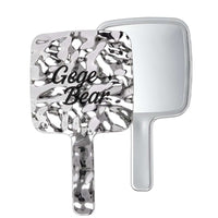 Handheld mirror with decorative handle and 'Gege Bear' text on a white background