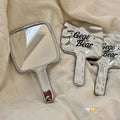 Two handheld mirrors with 'Gege Bear' branding on a beige fabric background