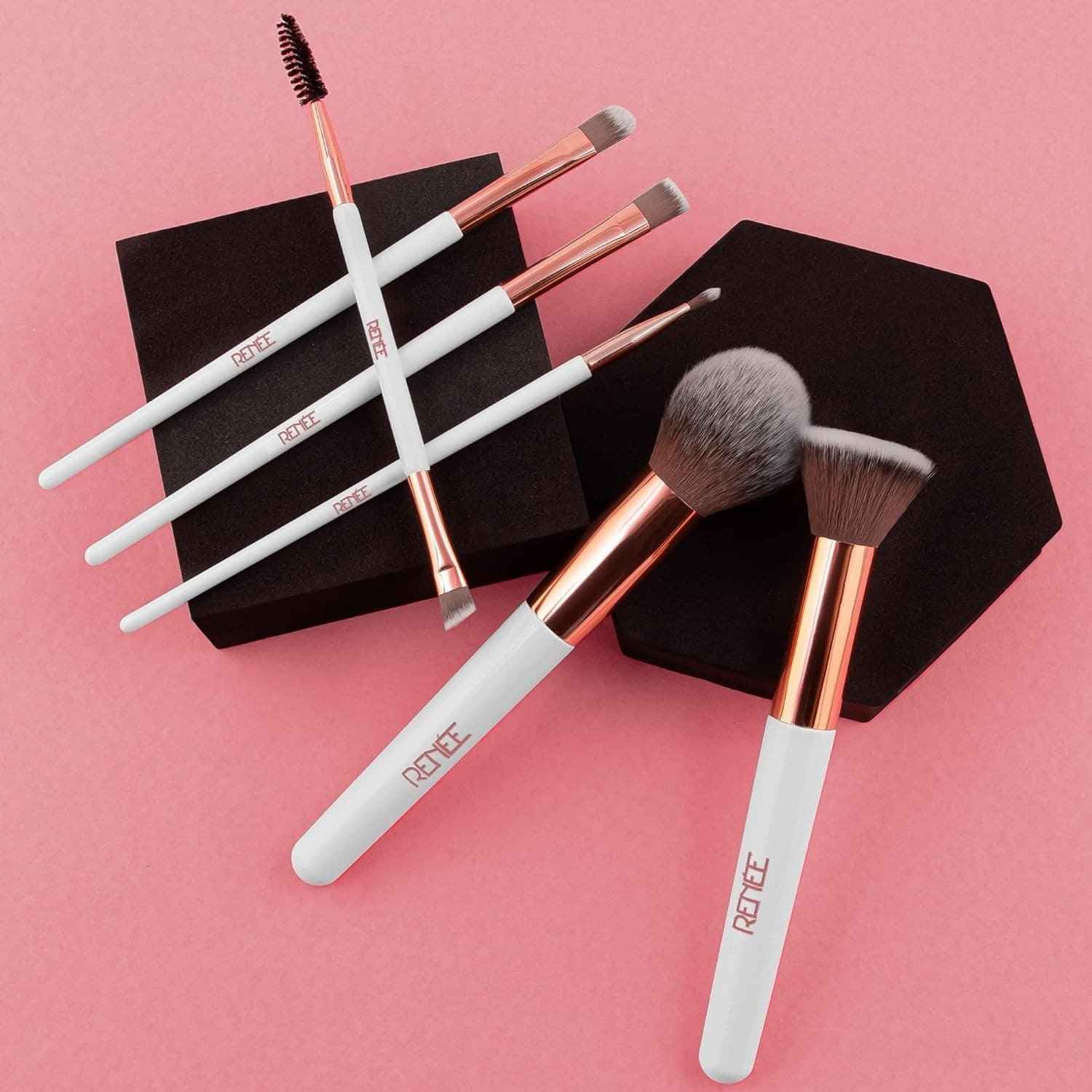 Makeup brushes with rose gold and white handles on a pink background