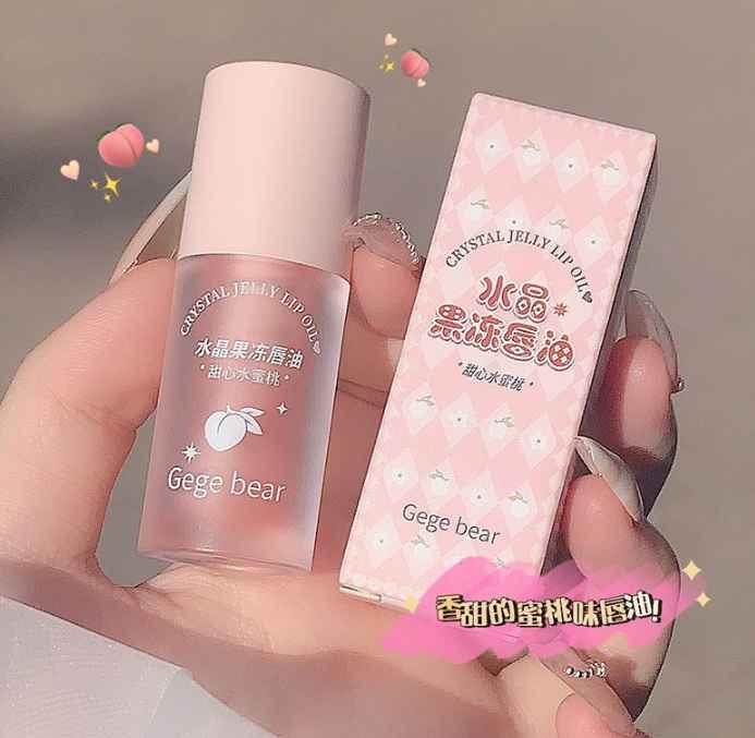 gege bear Lip oil with packaging held by a hand on a plain background in peach color 