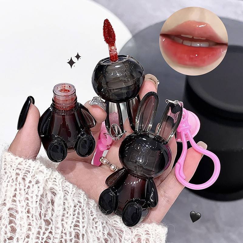 Black rabbit-shaped lip gloss held by a hand with a close-up of lips wearing the product.