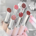 Set of lip glosses with various shades held by a hand against a blurred background