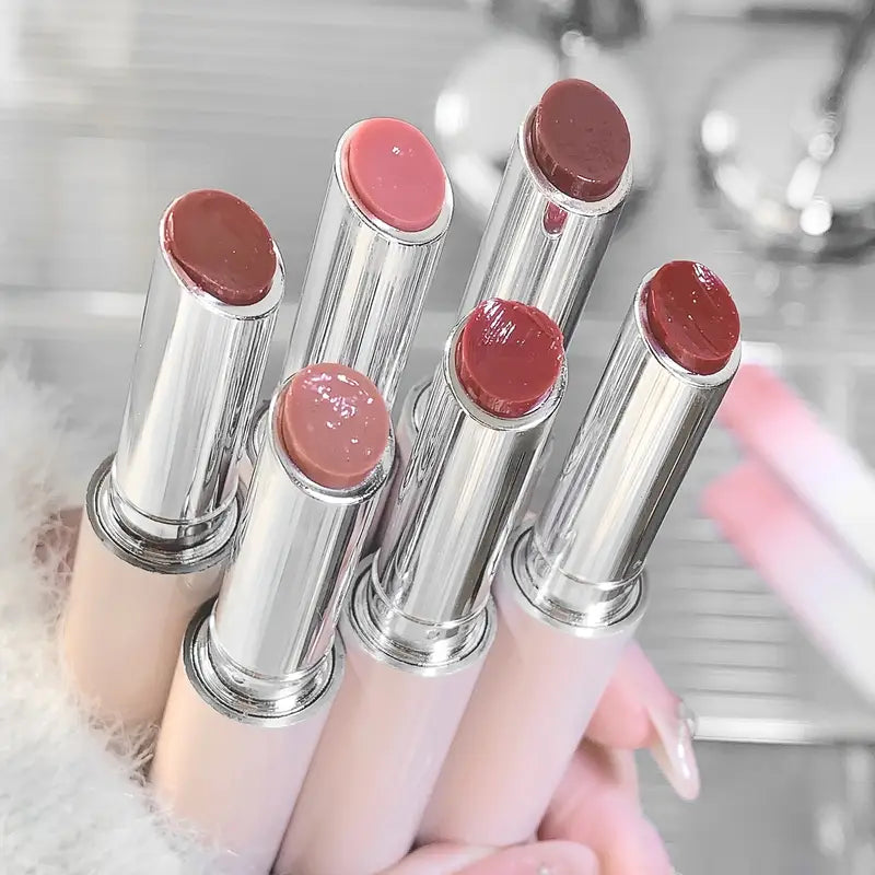 Set of lip glosses with various shades held by a hand against a blurred background