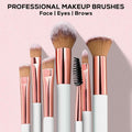 Set of professional makeup brushes with rose gold and white handles on a pink background.