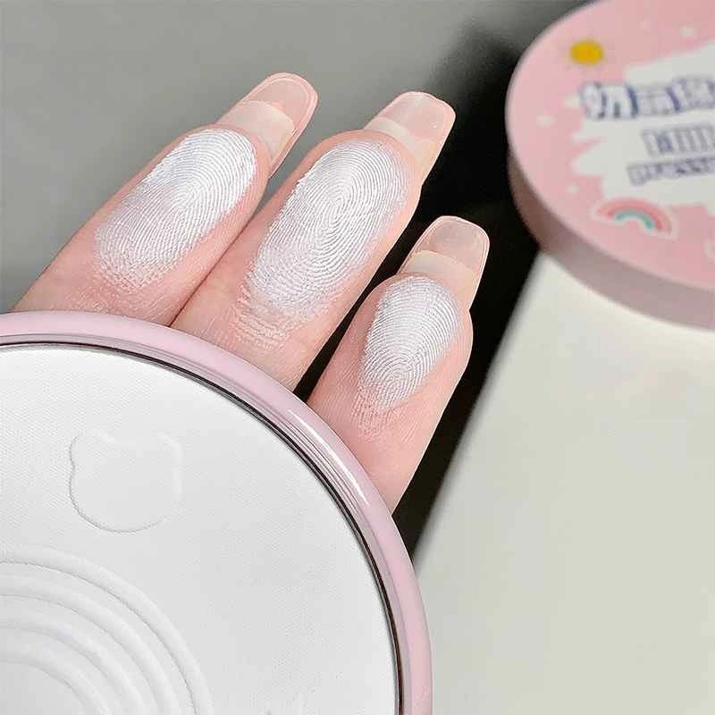 Hand with white compact on fingers next to a pink container